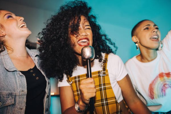 Karaoke time. Vibrant young woman singing into a microphone while partying with her friends at night.  Group of happy female friends having a good time together on the weekend.